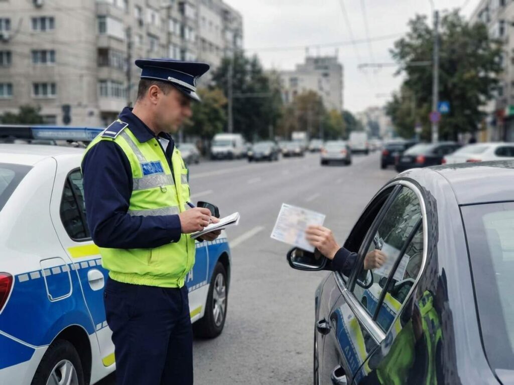 Politist rutier langa autospeciala, verificand documentele unui conducator auto, ilustrand contraventia de neprezentare la invitatia politiei rutiere