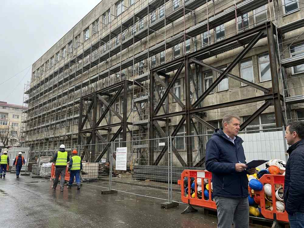 Spital public din România în lucrări de consolidare seismică, schele și contravântuiri metalice pe fațadă, inginer cu clipboard