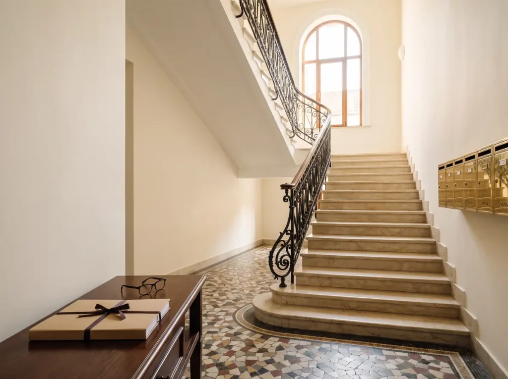 Hol de intrare intr-o cladire interbelica restaurata din Bucuresti, cu scara de marmura, balustrada de fier forjat si un dosar de acte legat cu panglica pe o consola