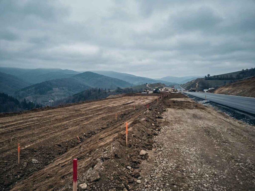 Peisaj deluros lângă un șantier de autostradă, teren defrișat pentru un amplasament suplimentar de expropriere