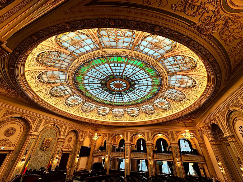 Sala de plen a Senatului României din Palatul Parlamentului, cu cupola de vitraliu, stema țării și drapelul pe perete