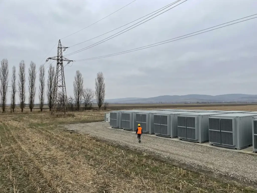 Șir de containere de stocare în baterii pe un teren agricol din România, lângă o linie electrică, ilustrare pentru ghidul de finanțare din Fondul pentru modernizare
