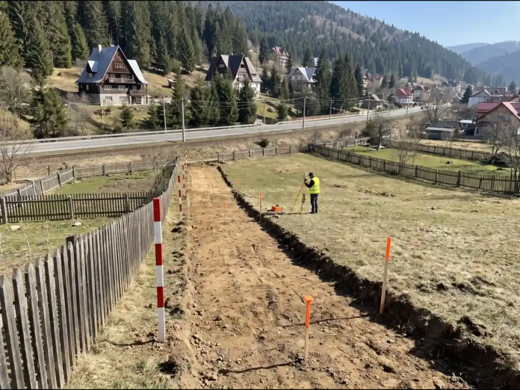 Coridor de expropriere jalonat prin grădini și fânețe la marginea unui oraș montan din Prahova, cu terasament nou alături