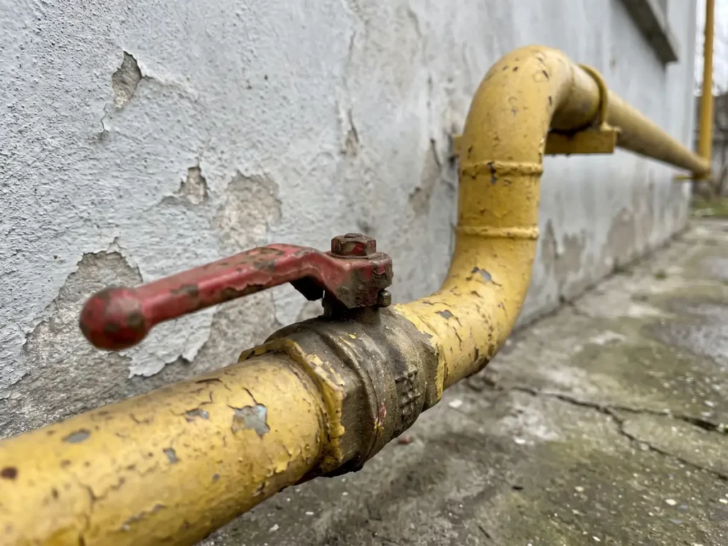 Tevi galbene de gaz pe peretele unei case, cu robinet de inchidere cu maneta rosie