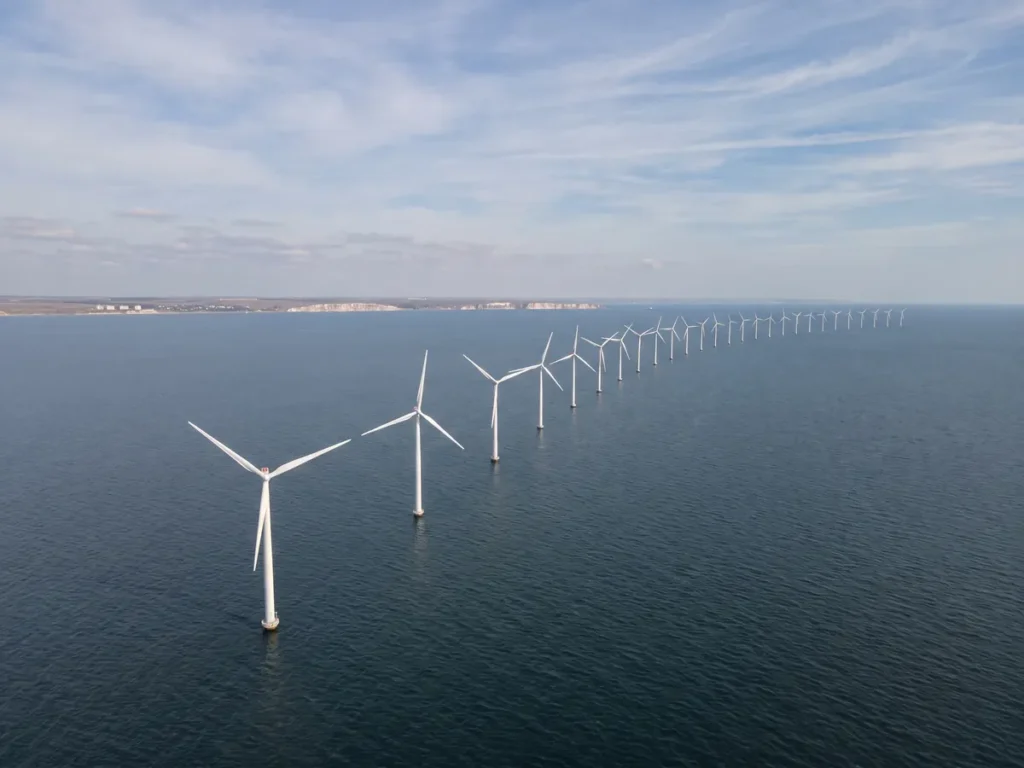 Turbine eoliene offshore aliniate în apele Mării Negre, văzute de sus, cu linia țărmului românesc în depărtare.