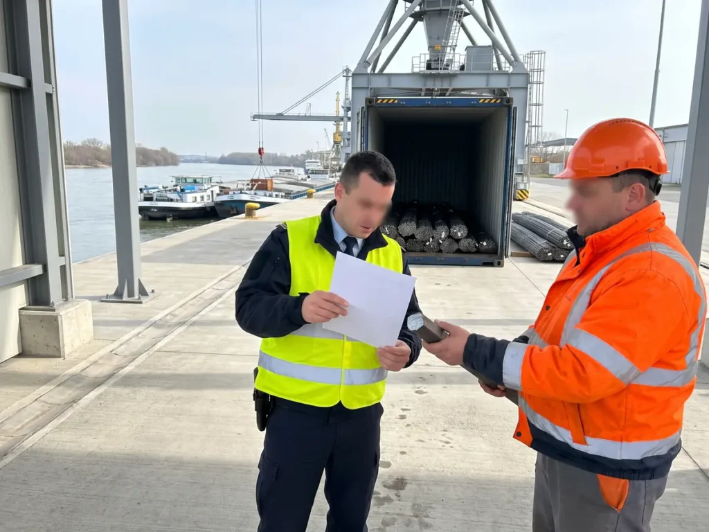 Vameș comparând documentația de uzină cu marcajul de pe capătul unei bare de oțel, într-un port fluvial